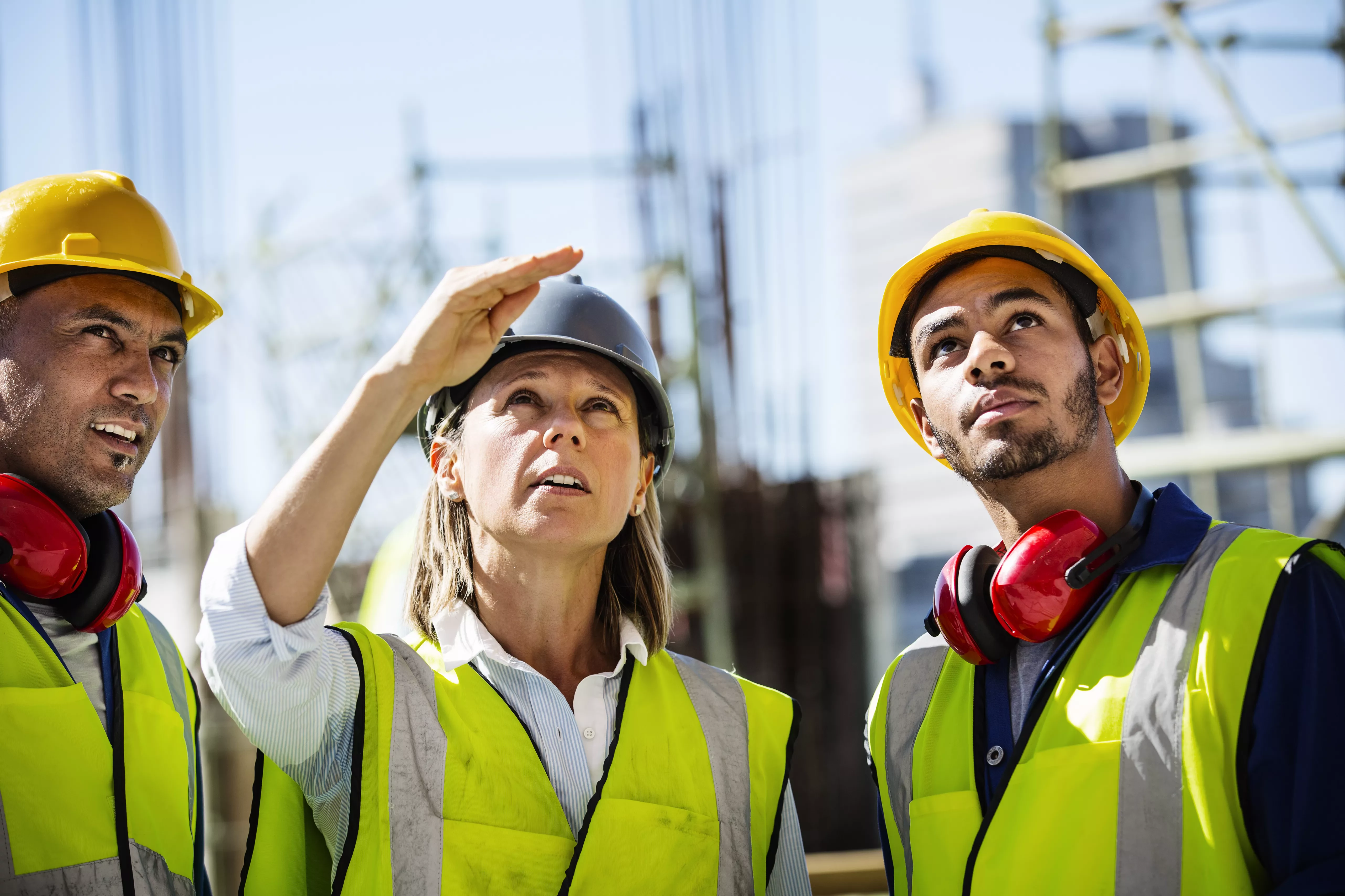 Group of construction workers in safety helmets and vests looking at a building site.