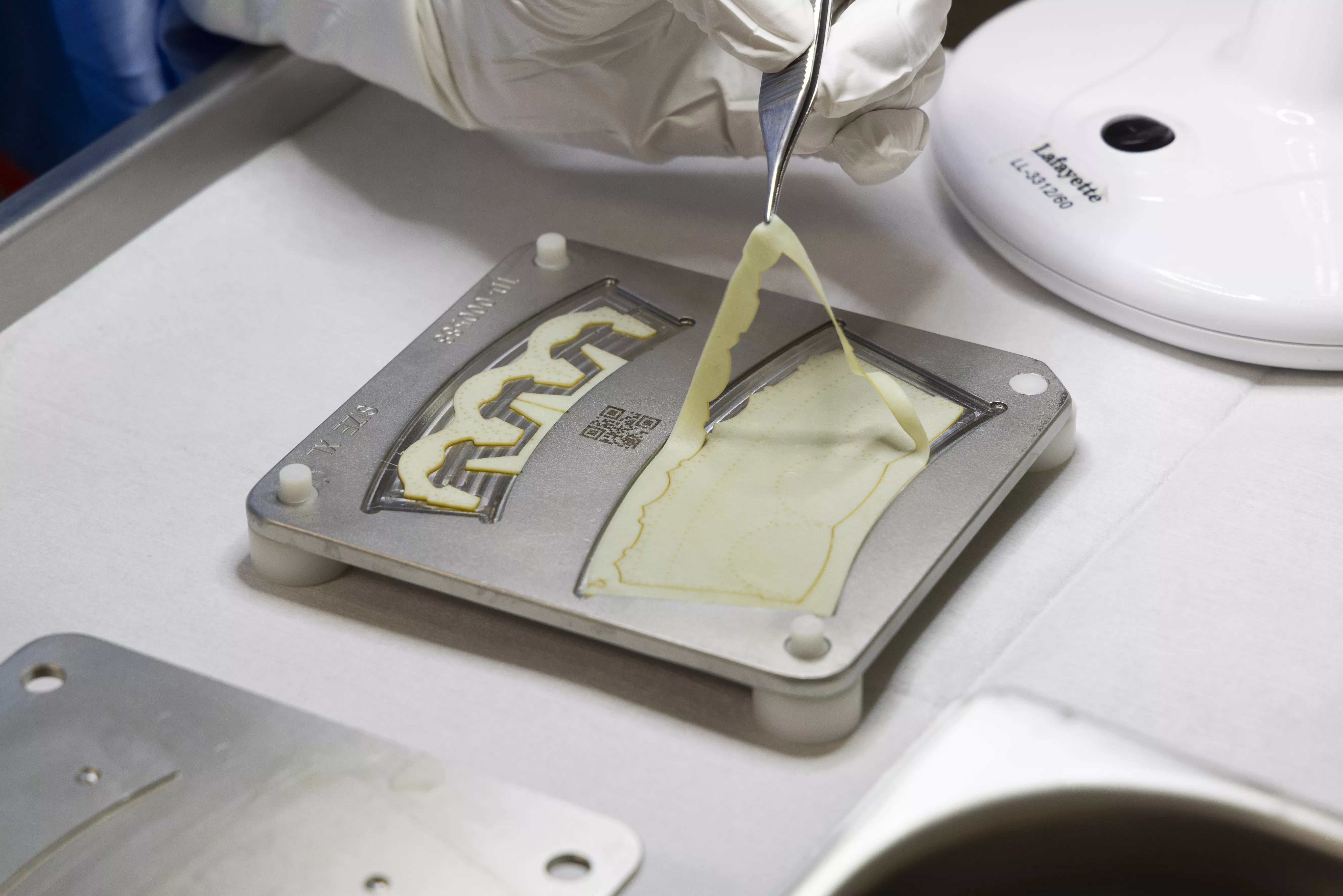 Gloved hand using tweezers to peel biomedical material from a mold, representing Corcym’s precision manufacturing of cardiovascular devices.