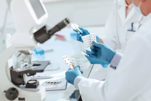 Scientists in a laboratory examining blister packs of pills next to a microscope.
